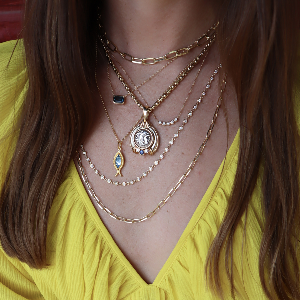 Photo of a woman wearing several necklaces with a yellow shirt.